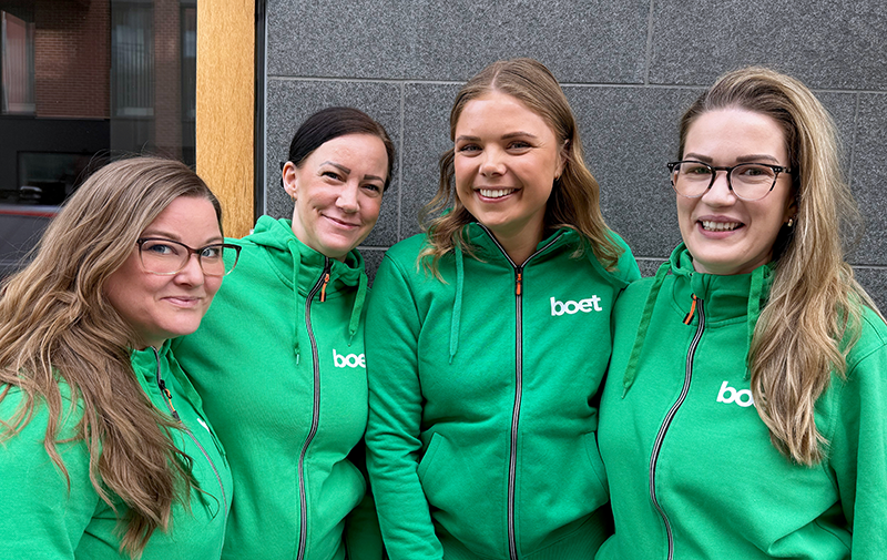 Fyra kvinnor i gröna luvtröjor ler mot kameran.